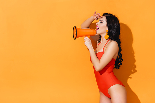 excited young woman in swimsuit holding megaphone on orange
