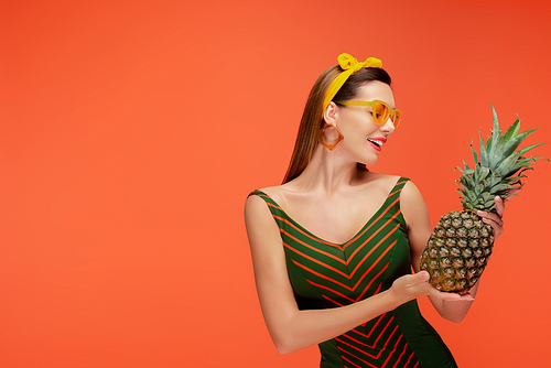 Woman smiling and looking at pineapple isolated on orange