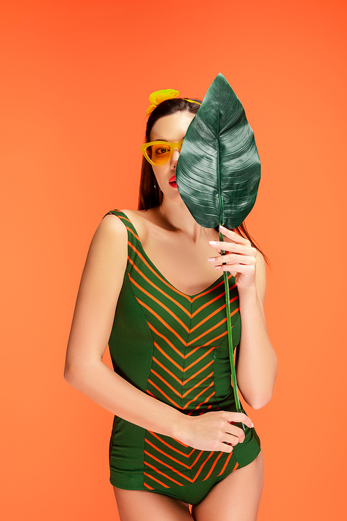 Front view of woman covering face with leaf isolated on orange