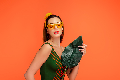 Woman with closed eyes holding leaf isolated on orange