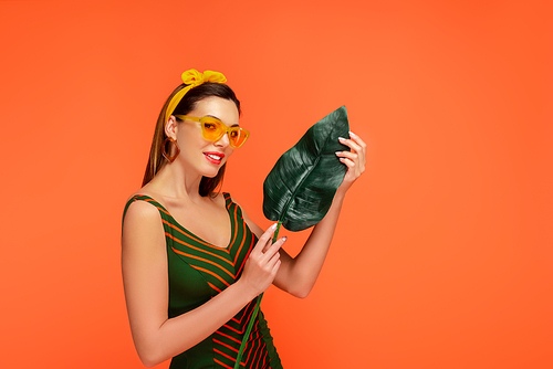 Woman smiling,  and showing leaf isolated on orange