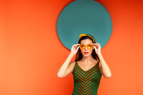 Woman touching sunglasses and  with blue circle behind on orange background