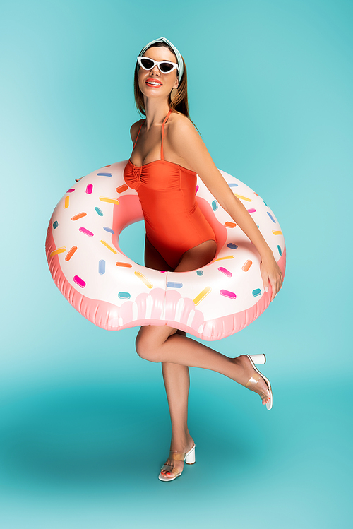Woman with inflatable ring raising leg and smiling on blue background