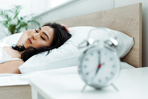 selective focus of asian woman sleeping near alarm clock