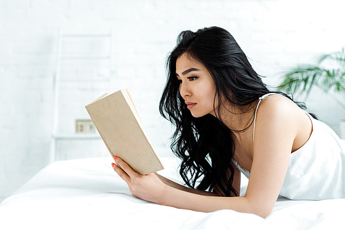 pretty asian woman lying on bed and reading book