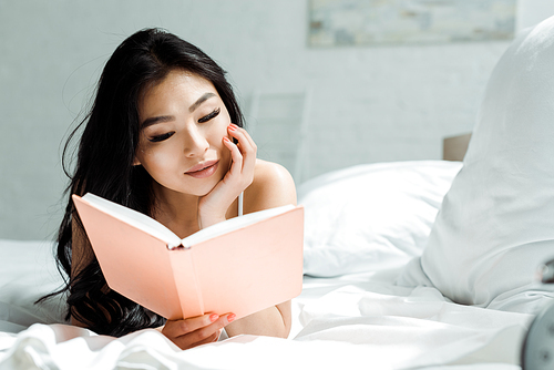 attractive thai woman reading book and lying on bed at home