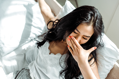 overhead view of asian woman with closed eyes covering face with yawning