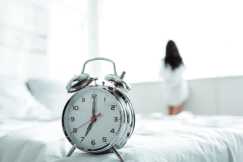 selective focus of alarm clock near brunette woman standing at home