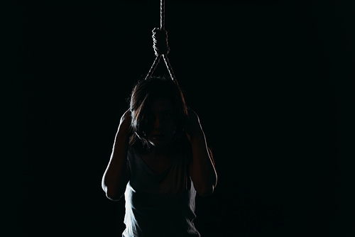 depressed woman committing suicide while putting noose on neck in darkness isolated on black
