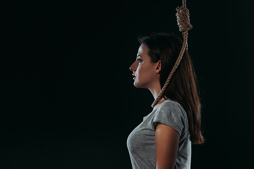 side view of depressed young woman going to commit suicide by hanging herself isolated on black