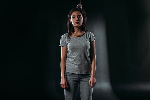 depressed young woman  while standing with noose on neck on black background