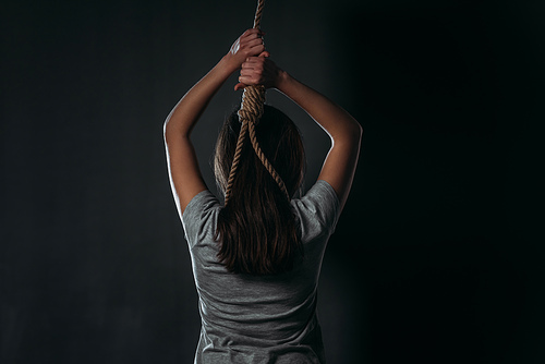 back view of woman committing suicide while putting noose on neck on black background