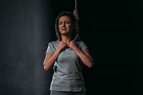 depressed, crying woman committing suicide while putting noose on neck on black background