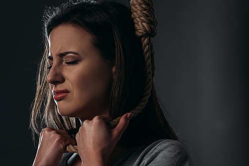 frustrated, crying woman committing suicide while putting noose on neck on black background