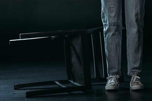 cropped view of woman standing near fallen chair on black background