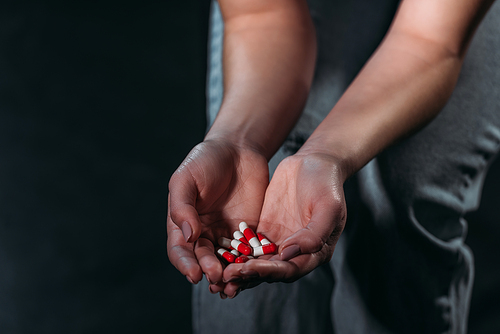 partial view of depressed woman holding handful of pills and going to commit suicide isolated on black