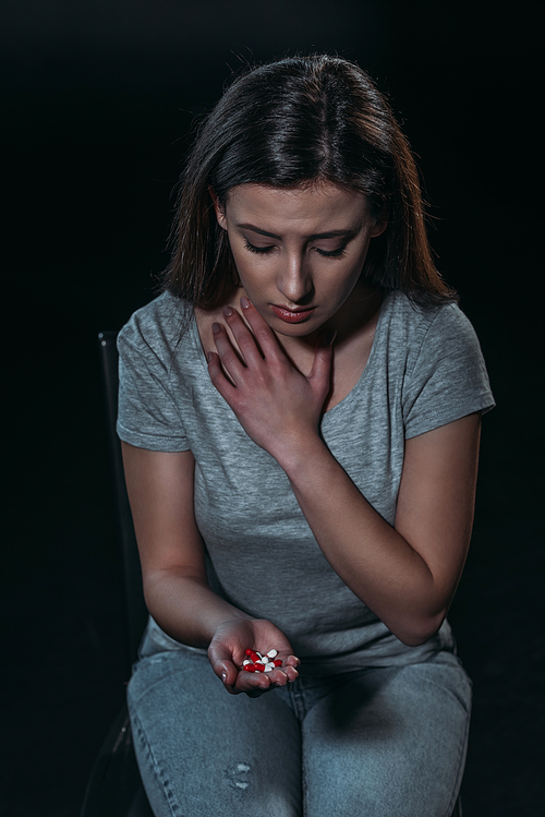 frustrated woman holding handful of pills and going to commit suicide isolated on black
