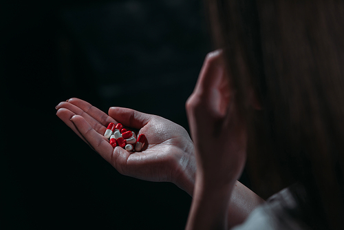 partial view of woman going to commit suicide and holding handful of pills isolated on black isolated on black