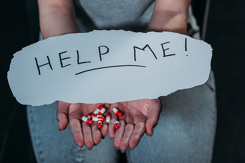 cropped view of woman with handful of pills and paper with help me inscription isolated on black