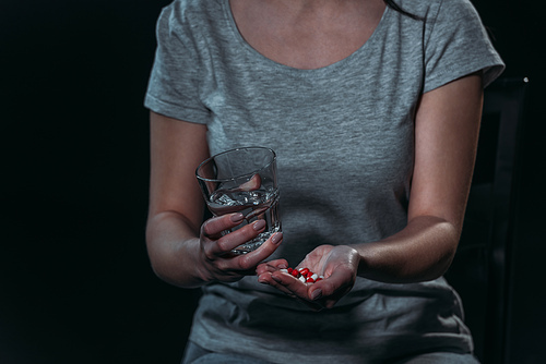 cropped view of woman going to commit suicide and holding handful of pills and glass of water isolated on black isolated on black