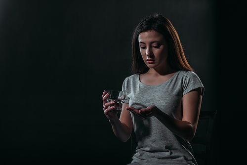 depressed woman going to commit suicide while holding handful of pills and glass of water isolated on black