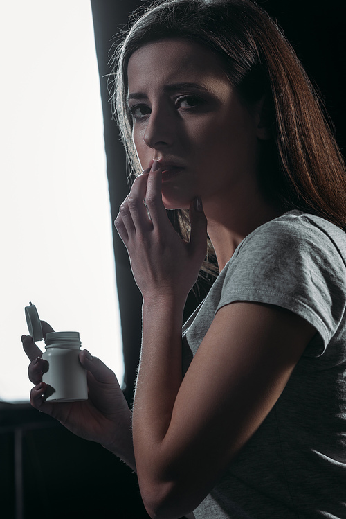 depressed woman  while holding container with pills and going to commit suicide on dark background with lighting