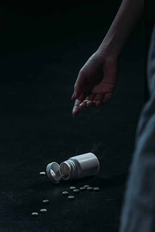 cropped view of hand of unconscious woman committed suicide by overdosing pills on dark background