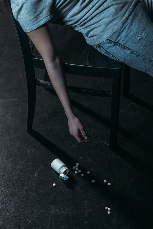 cropped view of unconscious woman committed suicide by overdosing pills on dark background