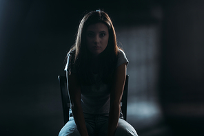 hopeless young woman  while sitting on chair in darkness on black background