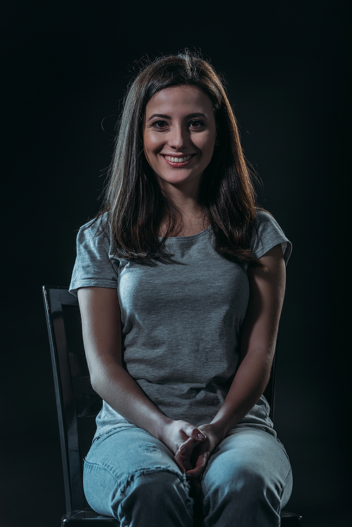 cheerful young woman  while sitting in darkness isolated on black