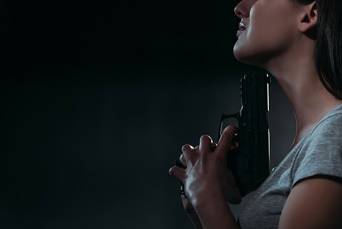 cropped view of depressed woman holding gun near chin on dark background