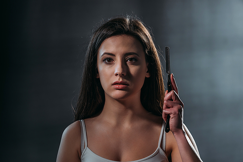 depressed young woman  while holding straight razor on dark background