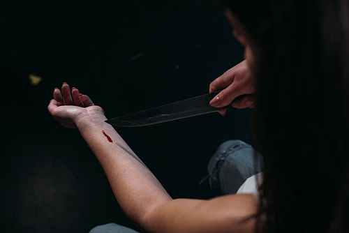 cropped view of woman committing suicide by cutting veins with knife isolated on black