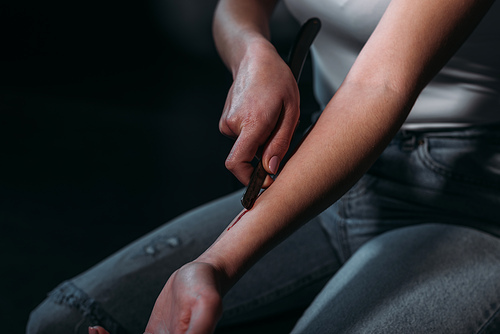 cropped view of woman committing suicide by cutting veins with straight razor isolated on black