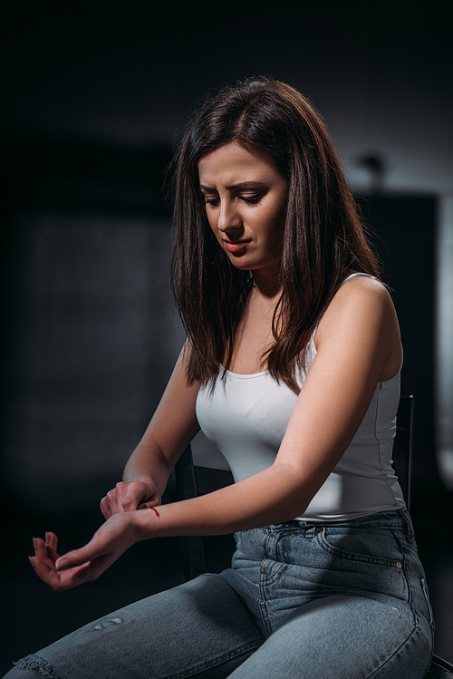 hopeless young woman committing suicide by cutting veins with straight razor on dark background