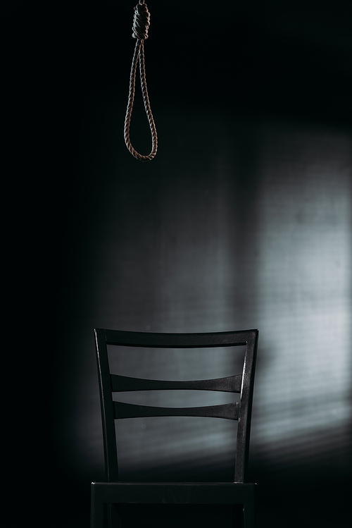 chair under hanging rope noose on black background with lighting, suicide prevention concept
