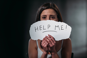 depressed woman  while holding paper with help me inscription on black background