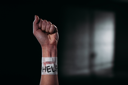 cropped view of female hand with word help on medical patches covering cut veins on black background with lighting