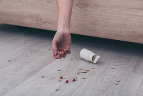 partial view of lifeless woman, committed suicide by overdosing medicines, lying on bed near scattered pills on floor