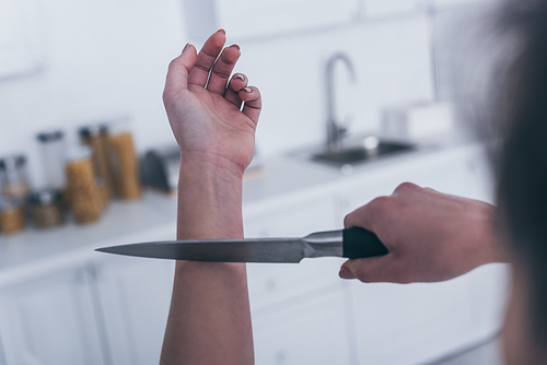 partial view of depressed woman committing suicide by cutting veins with knife in kitchen