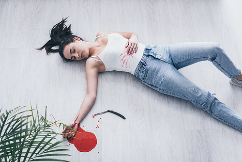 overhead view of lifeless woman with cut bleeding veins lying on floor near straight razor and puddle of blood