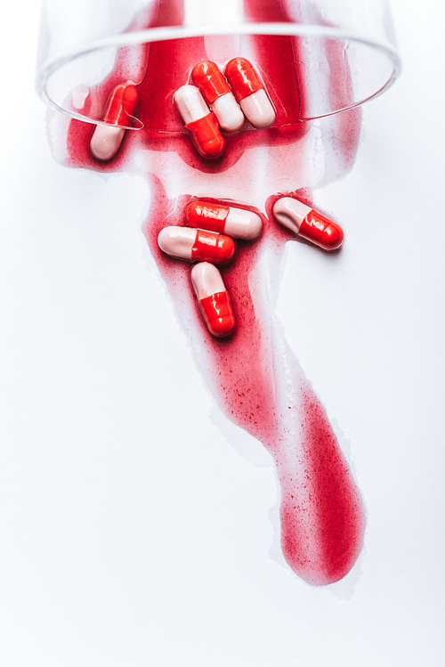 overturned glass and wet pills in red spills of water on white background, suicide prevention concept