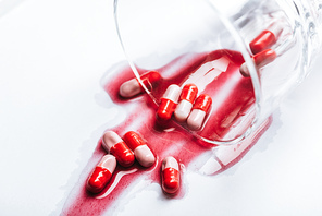 overturned glass and wet pills in red spills of water on white background, suicide prevention concept