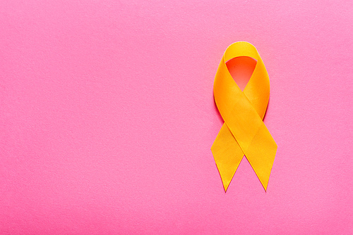 top view of yellow awareness ribbon on pink background, suicide prevention concept