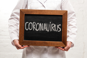 Cropped view of doctor holding chalkboard with coronavirus lettering on white background