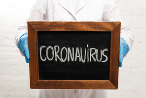 Cropped view of doctor holding blackboard with coronavirus lettering on white background