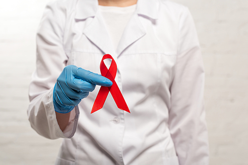 Cropped view of doctor in latex glove holding red ribbon of aids awareness on white background