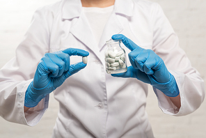 Cropped view of doctor holding jar and pill on white background