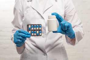 Cropped view of doctor holding jar and blister with pills on white background