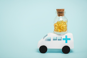Jar of pills on toy ambulance car on blue background